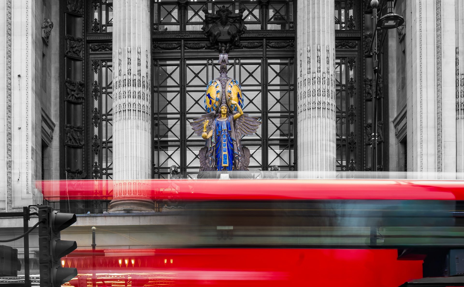 Selfridges London queen of time Vibrant statue in front of historic building with blurred red bus in motion.